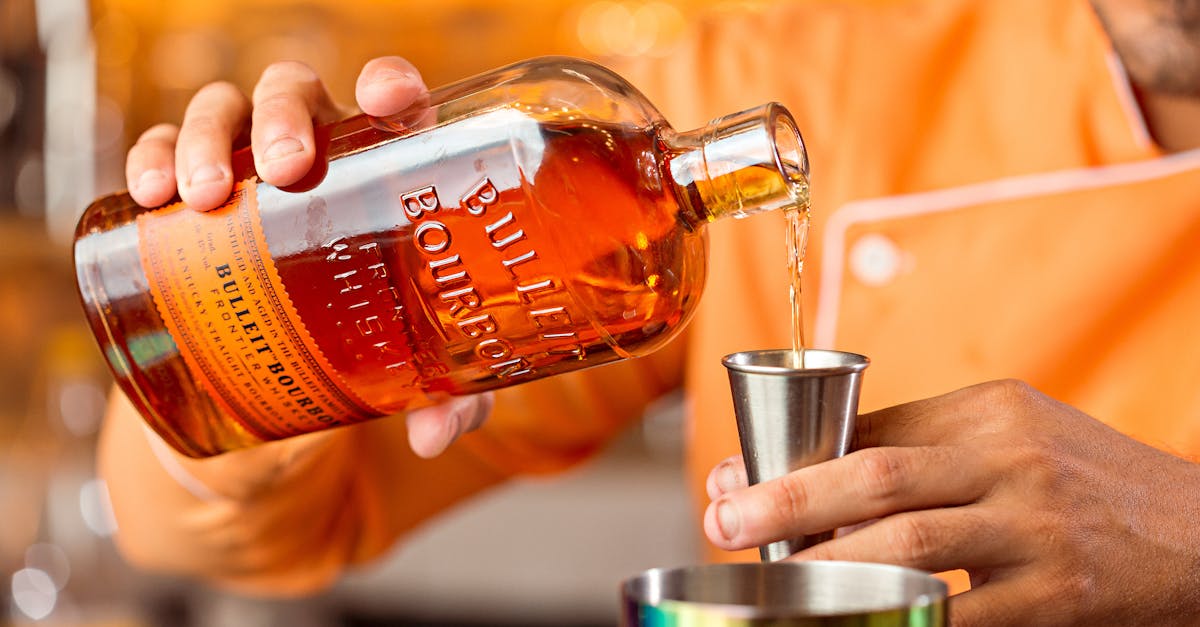 Person Holding a Bottle of Liquor and Stainless Jigger