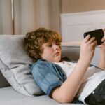 Young boy relaxing on a sofa, using a smartphone, indoors.